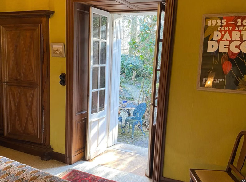 Porte-fenêtre ouverte sur un jardin ensoleillé.