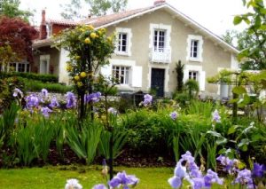 Maison entourée de fleurs et jardin verdoyant.